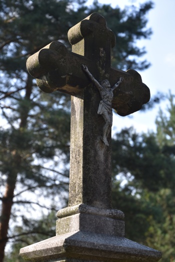 Na zdjęciu krzyż o ramionach zakończonych trójlistnie, na ramionach wyryte ozdoby w kształcie rozetek. Na krzyżu pasyjka z metalu (zdj. Katarzyna Mazur)